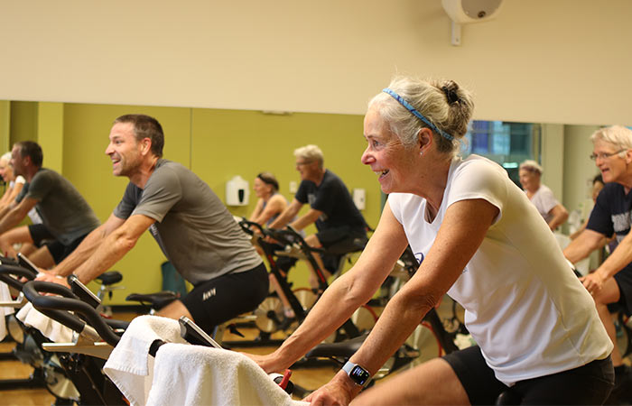 A group of adults smile while riding exercise bikes during a class at Magnuson Athletic Club